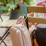 Denim Leather Bagnet holding a mauve purse, attached to the back of a metal chair in a green outdoor seating area