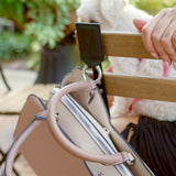 Noir Leather Bagnet holding a mauve purse, attached to the back of a metal chair in a green outdoor seating area